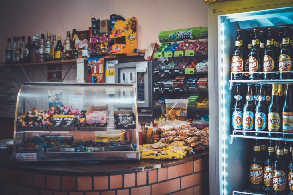 A well-stocked convenience store counter with snacks, drinks, and a refrigerator showcasing beverages.